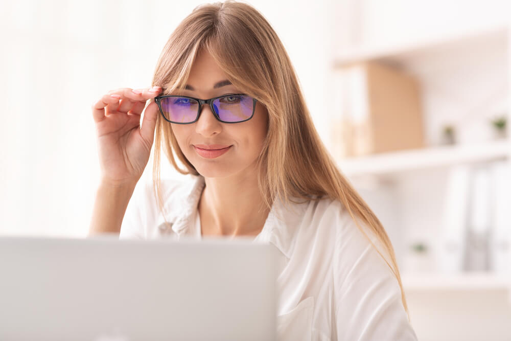 smiling woman wearing computer glasses at computer screen